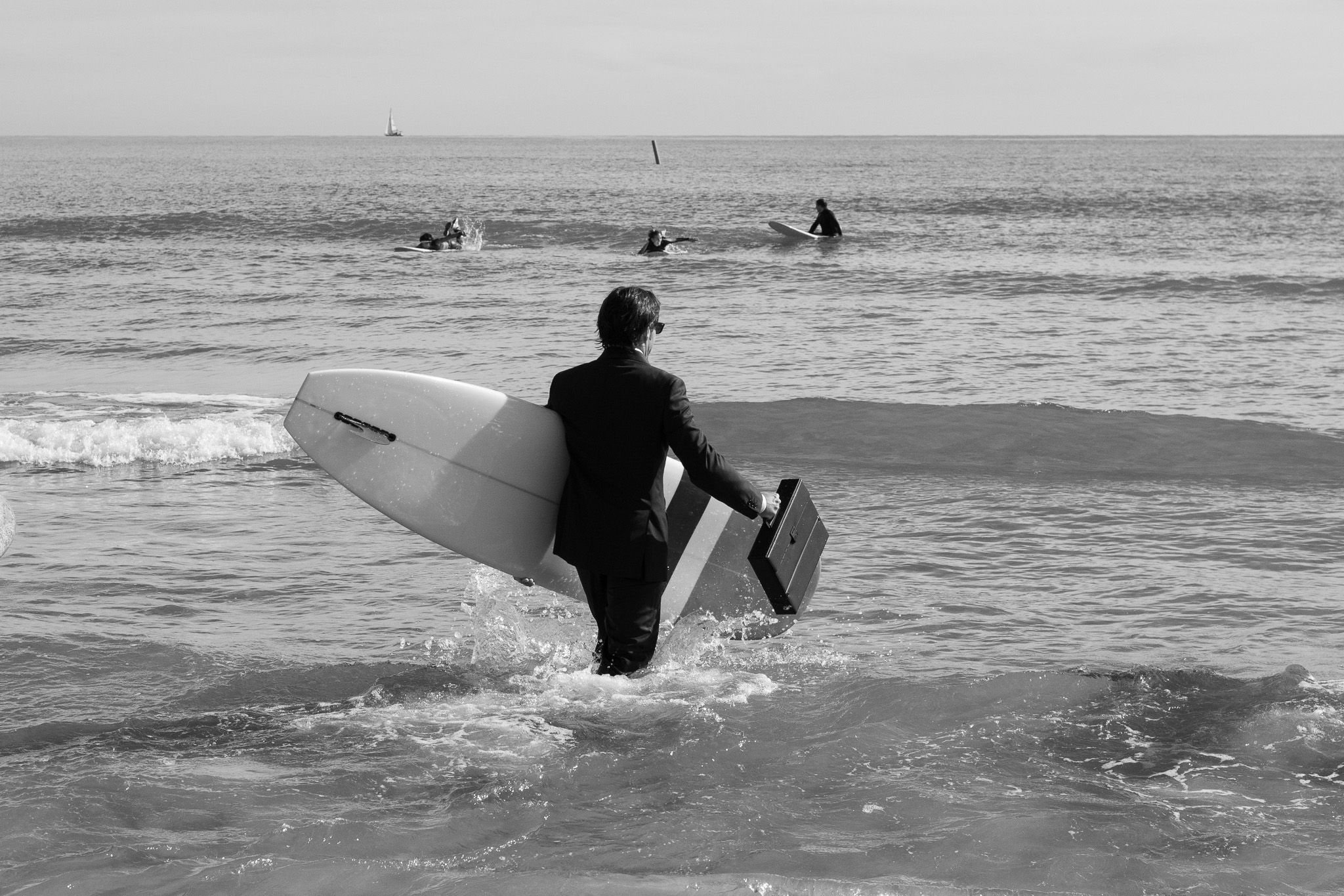 Contestant dressed as an executive entering the sea with a surfboard at the Quasimoto Festival