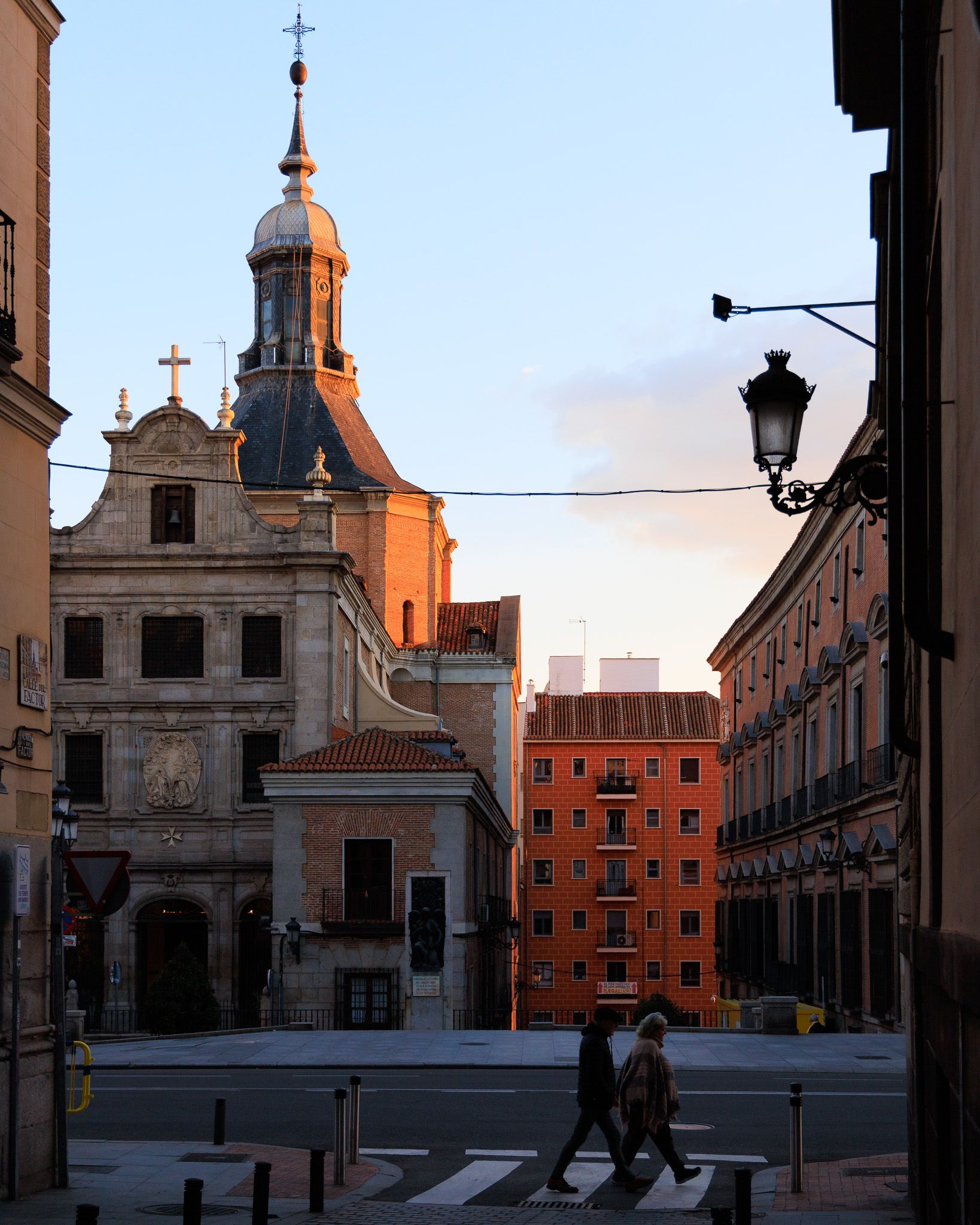 Two silhouettes crossing a pedestrian crossing in Madrid under the golden sunset light