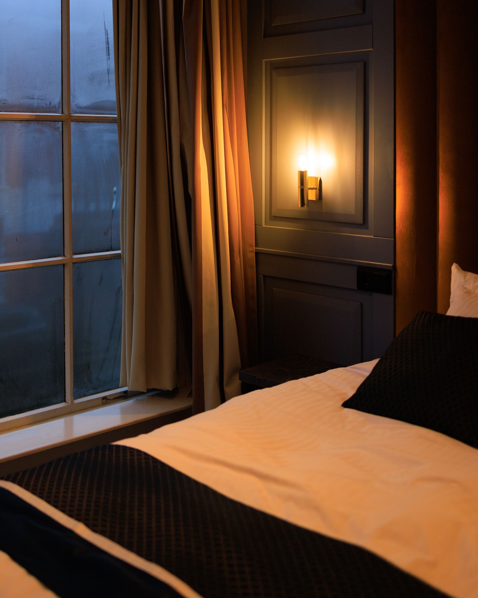 Interior of a room at the hotel The Royal Bridges in Delft with a lit lamp and fogged window