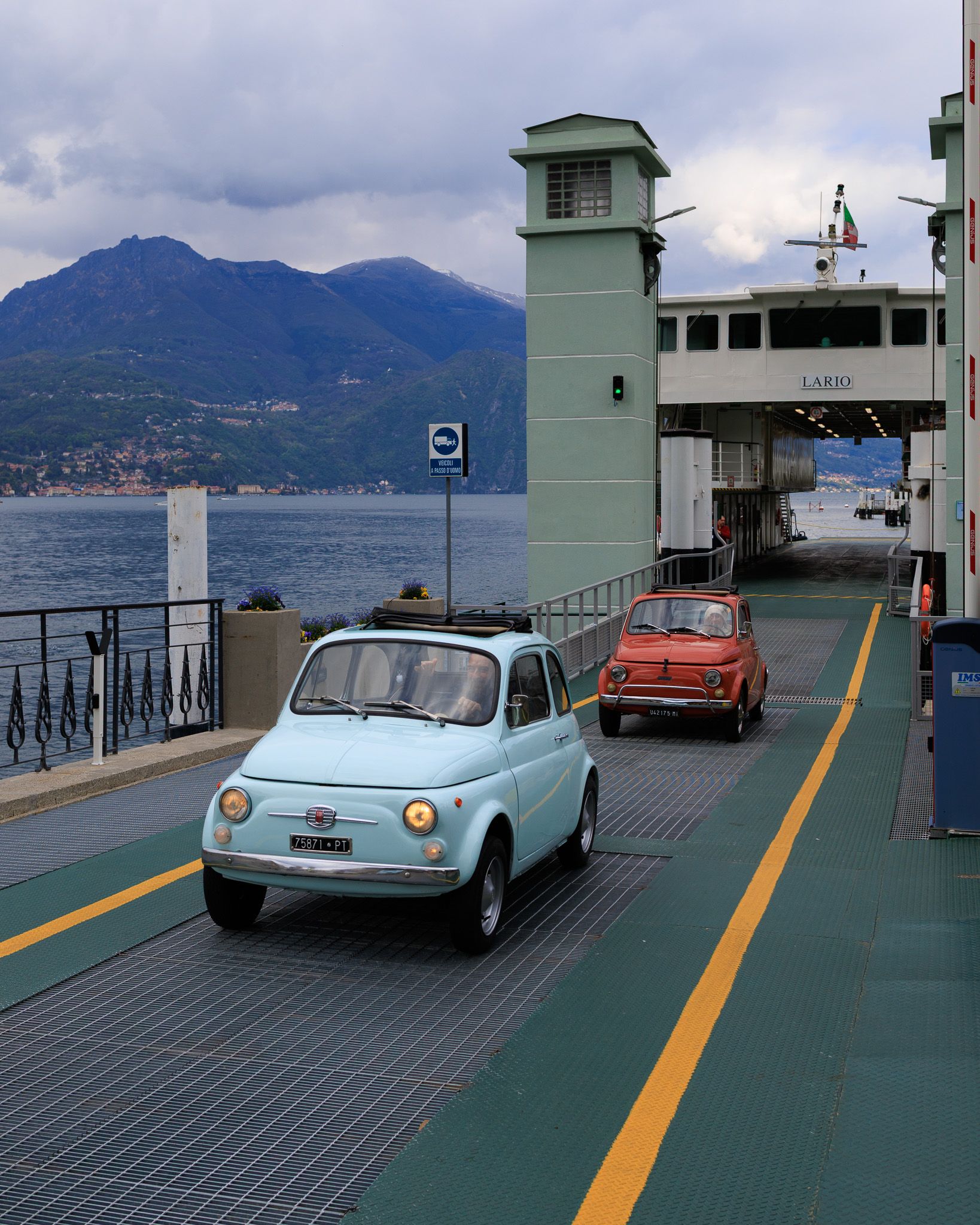 Two classic Fiat 500s, blue and red, descending from the ferry in Bellagio, Lake Como