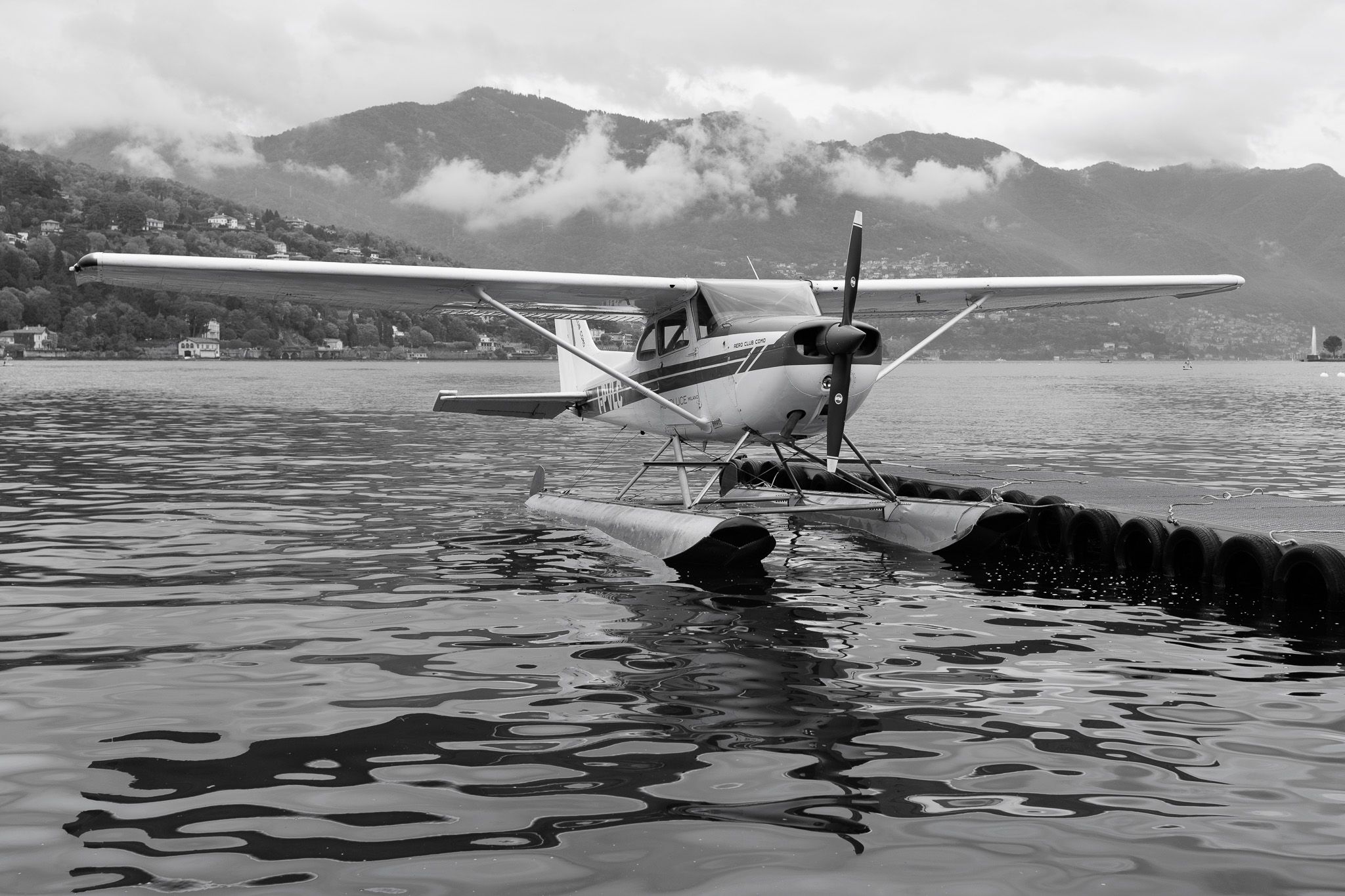 Aero Club Como seaplane on a floating platform with cloud-covered mountains behind