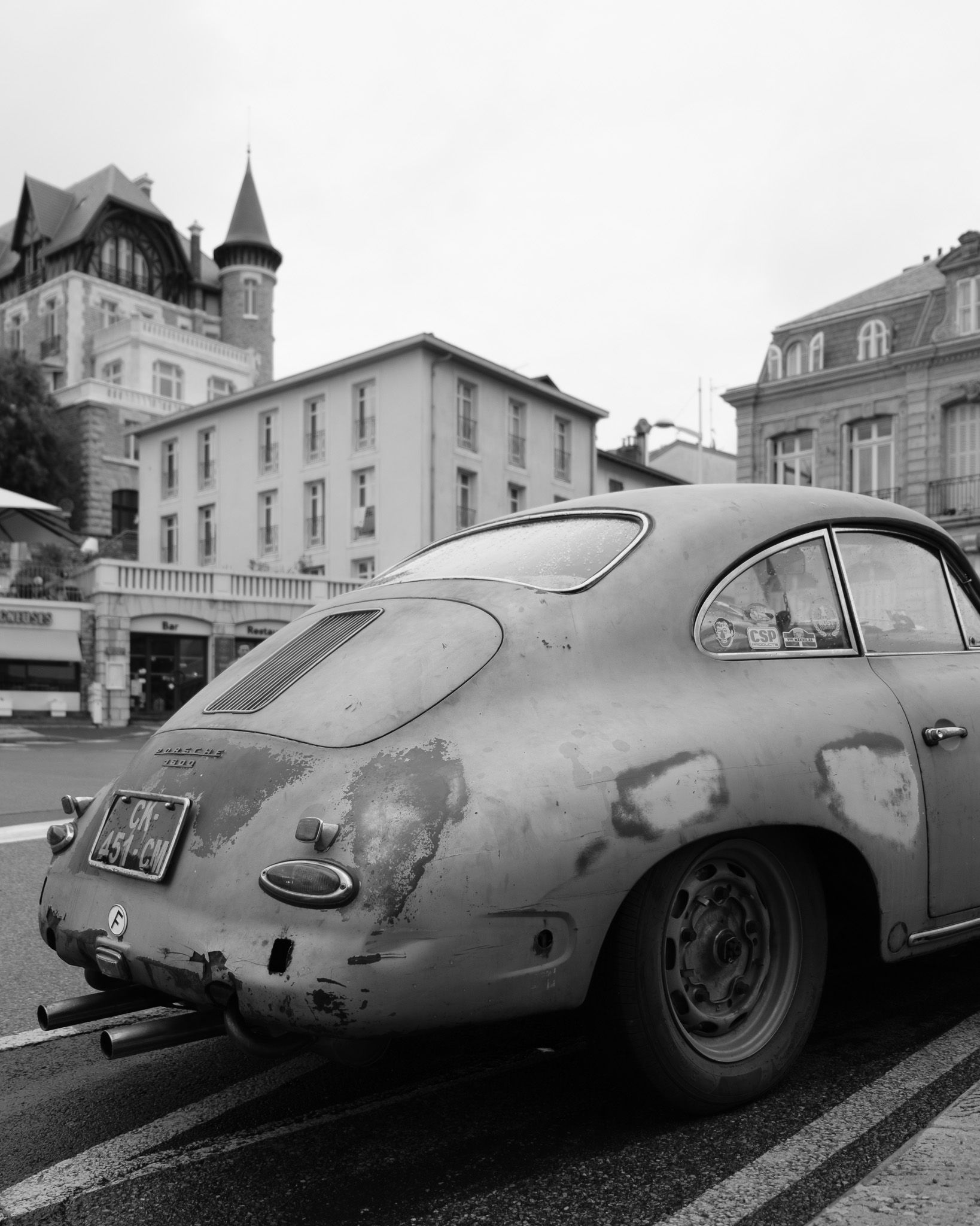 Weathered Porsche 356 on a street in Biarritz with classical architecture and wet pavement